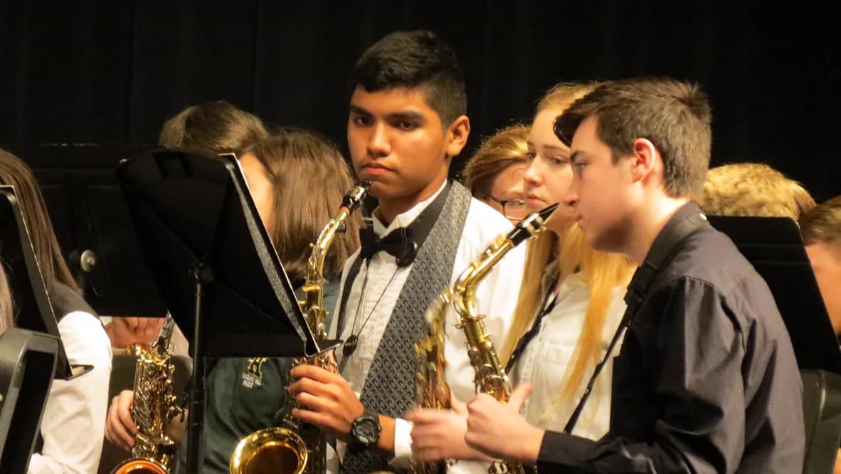 A younger Maximus Fernandez holding an alto saxophone during a school performance
